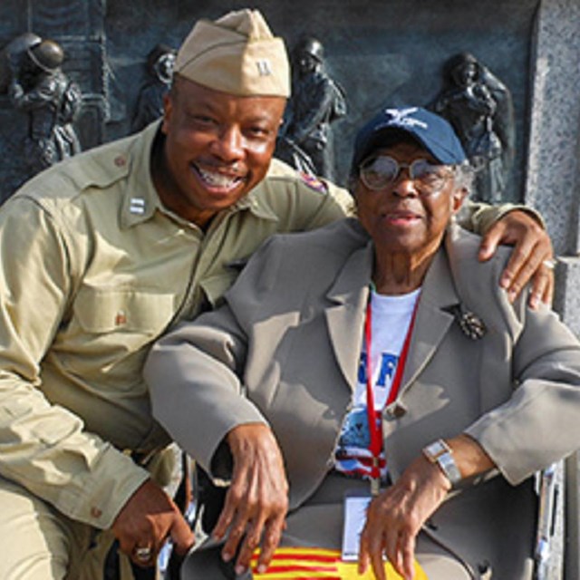 African American man in uniform with arm around older African American woman with medal and cap