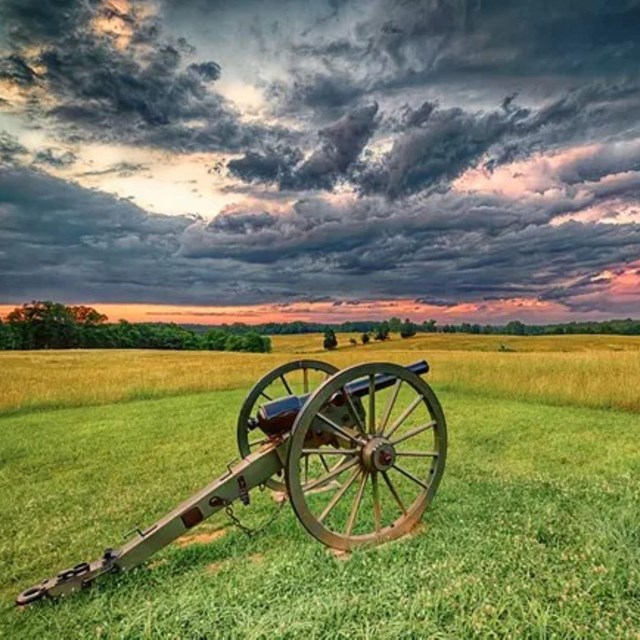 An old cannon sitting in a grassland with a sunset background. 