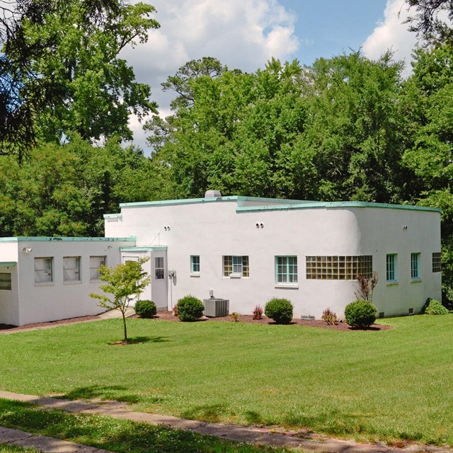 A white, flat-roofed house with a blue-green trim on the roof and windows