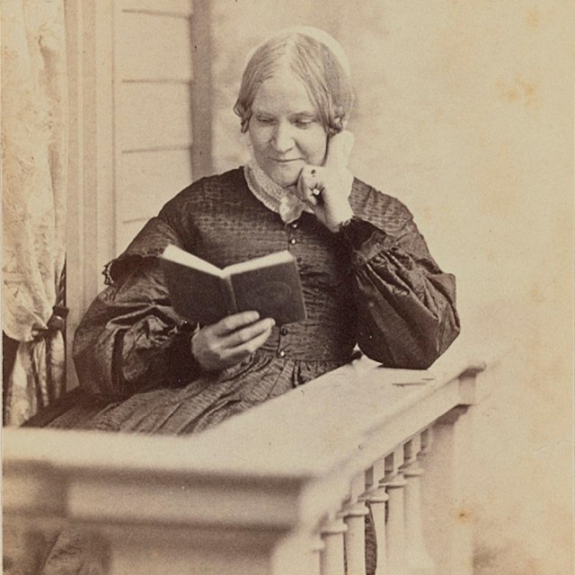 woman in a dress sitting on a balcony reading a book