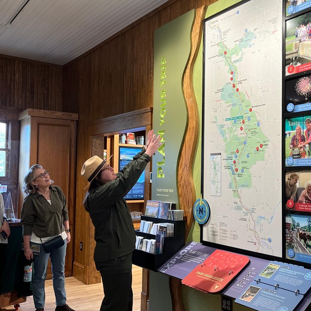 A park ranger pointing things out on a large park wall map