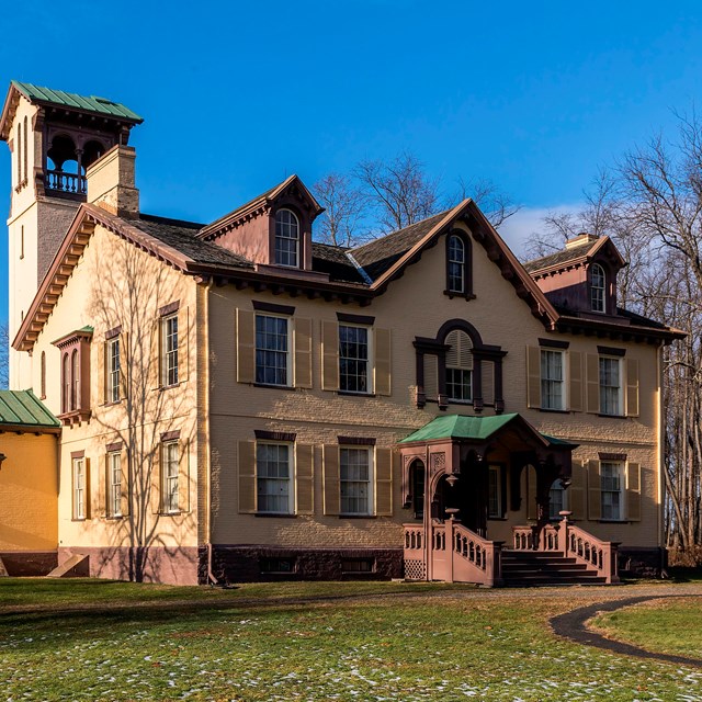 An elegant two-story tan brick building with a belltower on the backside.