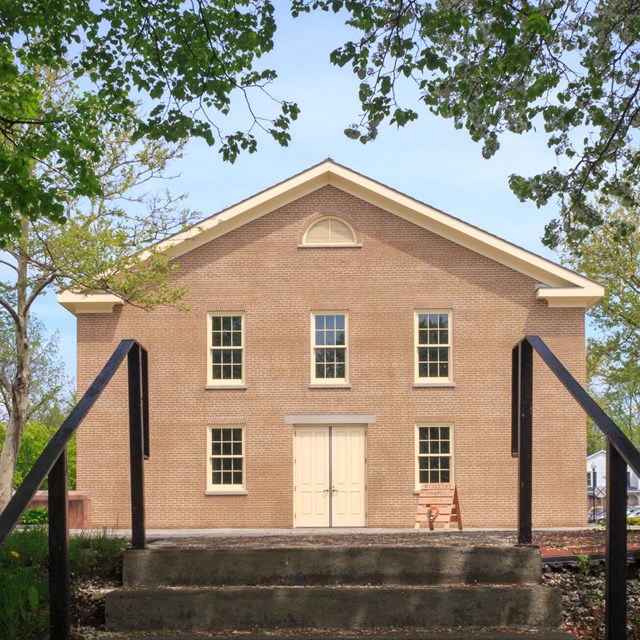 A square, two-story, red brick building with white-trimmed windows