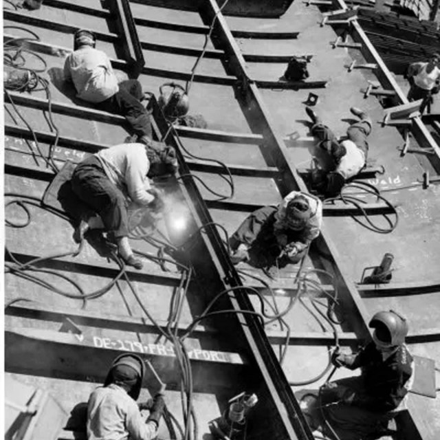 Women in face masks weld on the side of a large metal plate