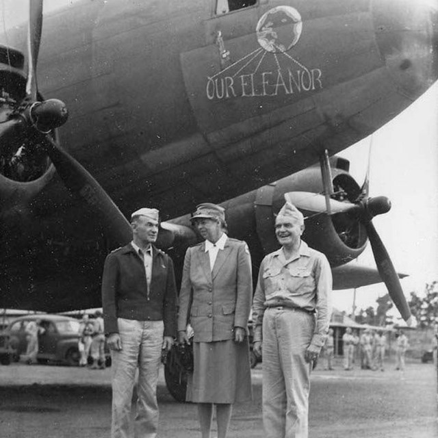 Two men and a woman stand in front of a plane which is painted with text 