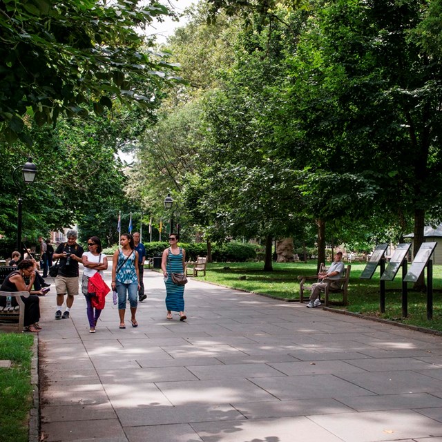 People stroll on a tree-lined path in an urban park.