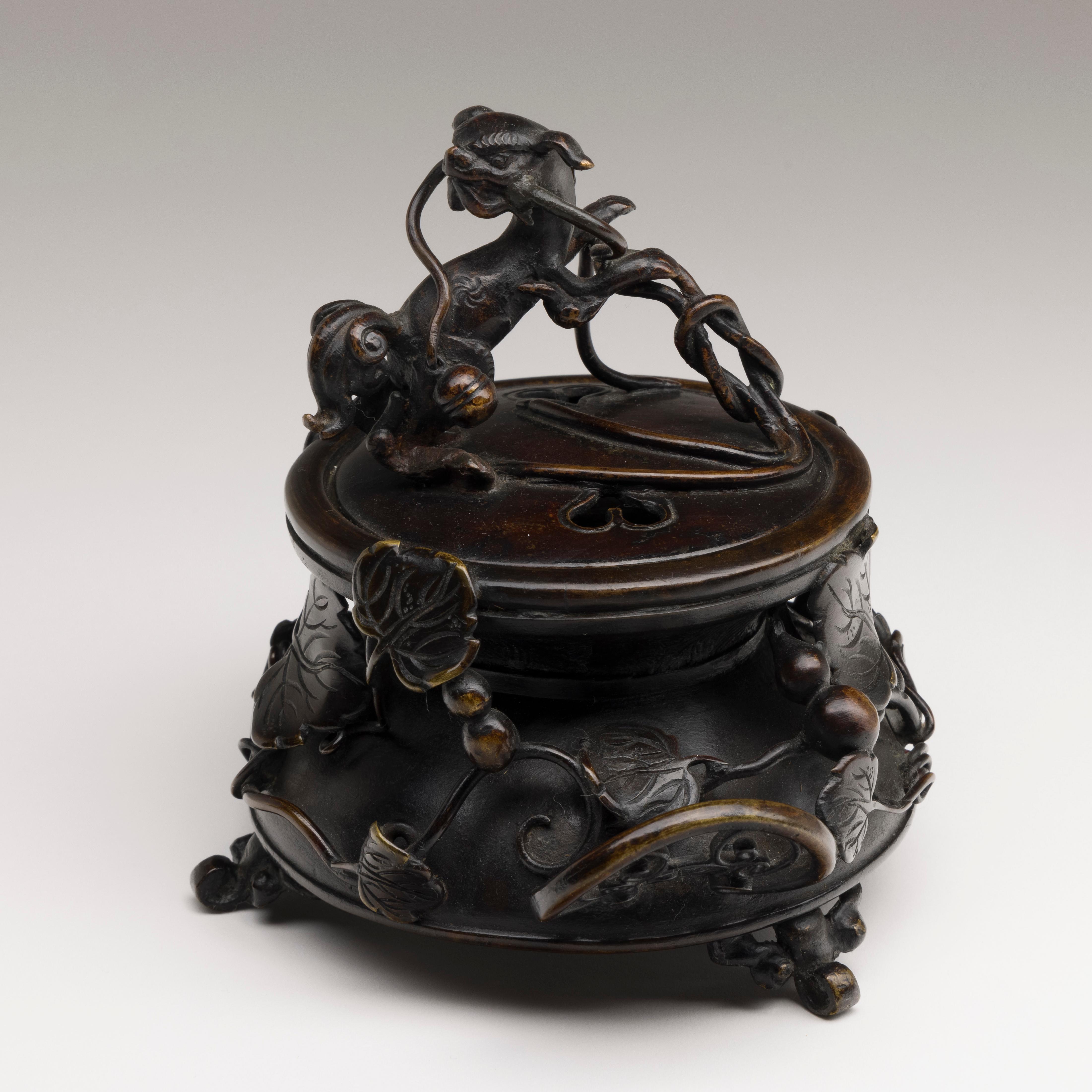 Bronze incense burner with raised vine decoration and sacred dog finial.