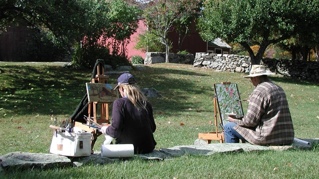 two people sitting on a lawn, painting