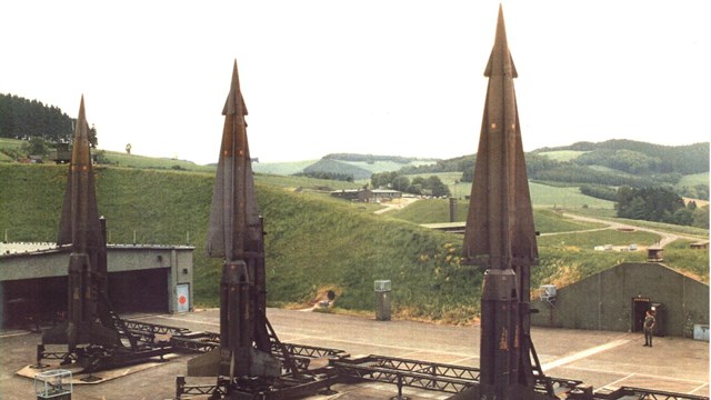 A trio of missiles stand upright and ready to fire from concrete pads