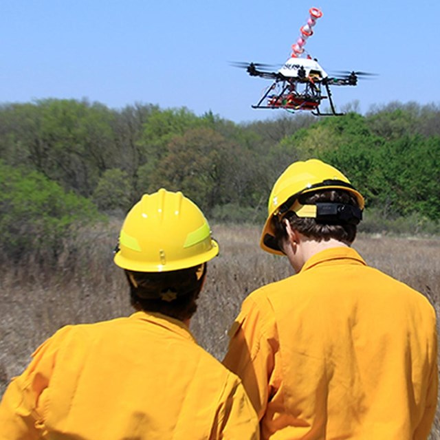 A man holds the controls for a stationary UAS while another man stand nearby.