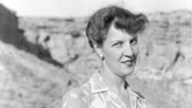 A woman (Florence Hawley Ellis) standing in a dress among remnants of sandstone walls. 