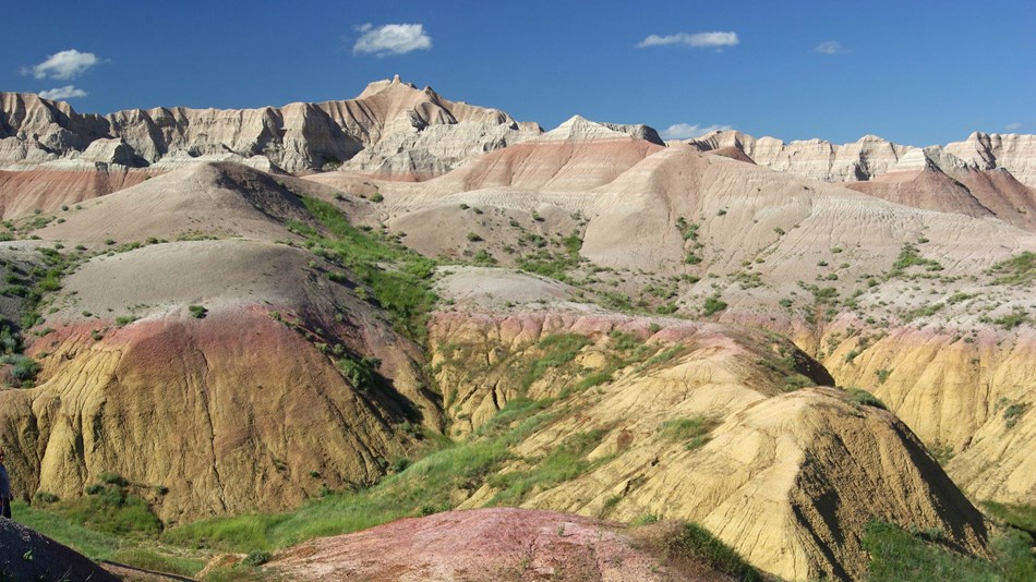 banded badlands buttes stretch far into the horizon with green prairie in valleys.