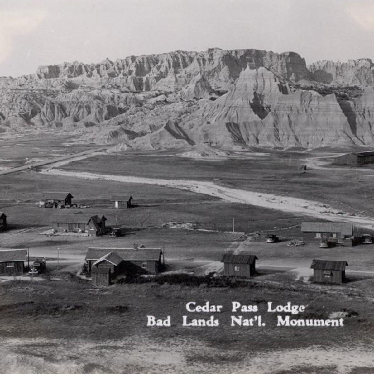 a historic black and white photo of a lodge and cabins in front of badlands buttes.