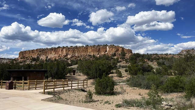A rocky mesa pictured against a bright blue sky with fluffy white clouds.