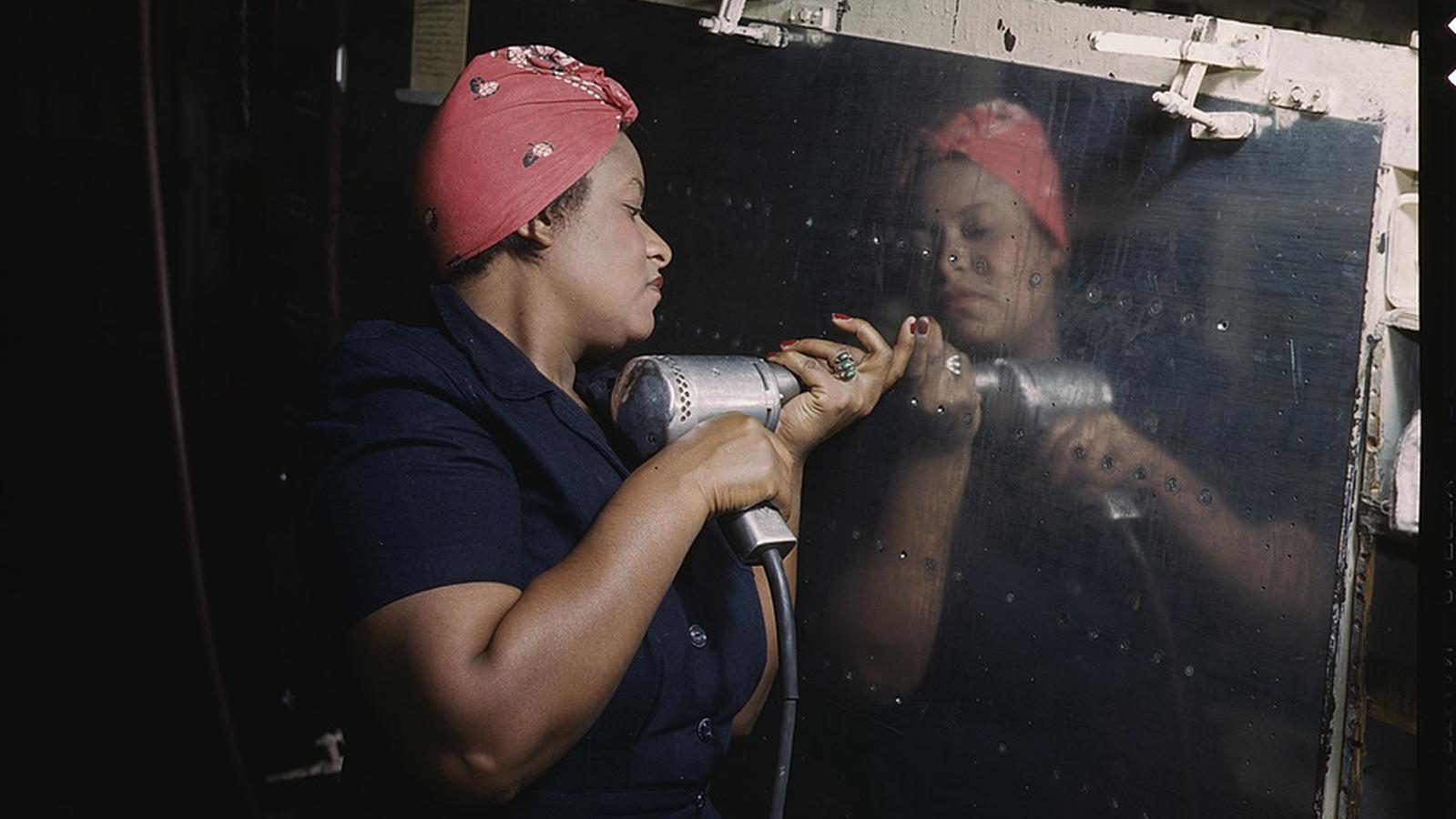 Black woman in red bandanna operates power drill on plane