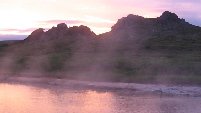 A small pool of water reflects a dusky sunset. 