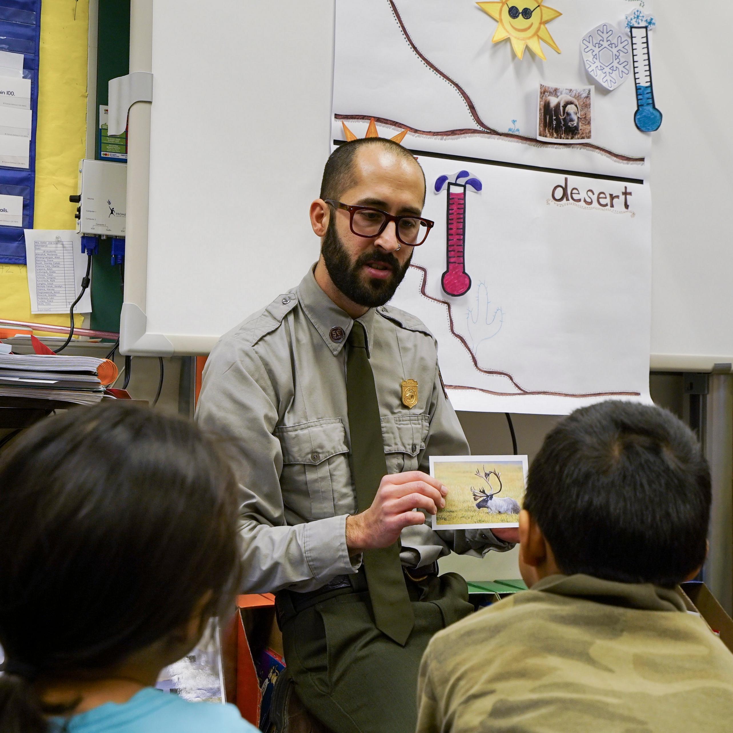 A park ranger holding an image of a caribou while speaking to a group of students.