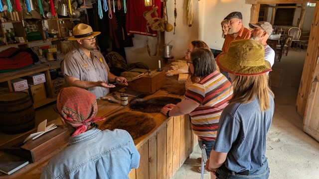 A park ranger speaks to visitors in the furnished trade room of the fort.  