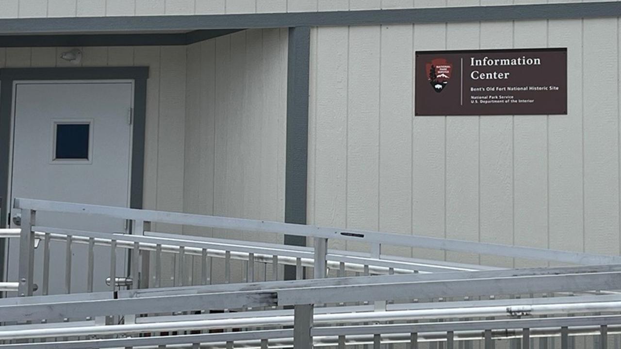 A metal ramp leads to the front door of a building with a brown identifying sign