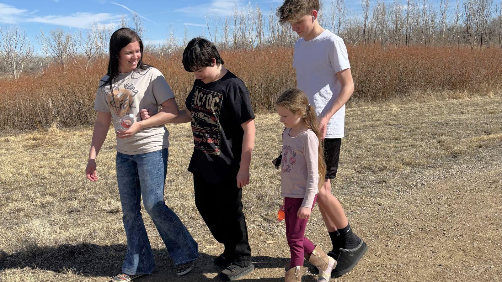 Mom with two teenagers and a young child walk along tall trail grasses