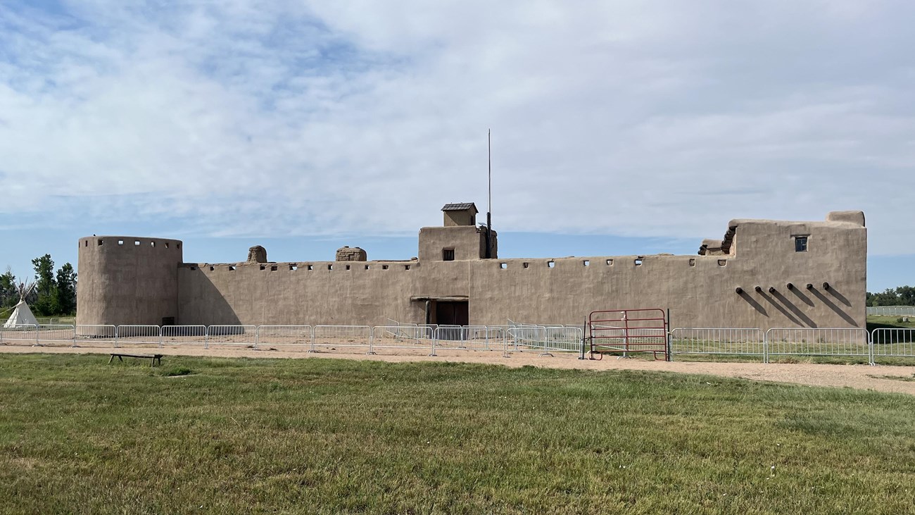 A safety fence surrounds a large, reconstructed fort. 