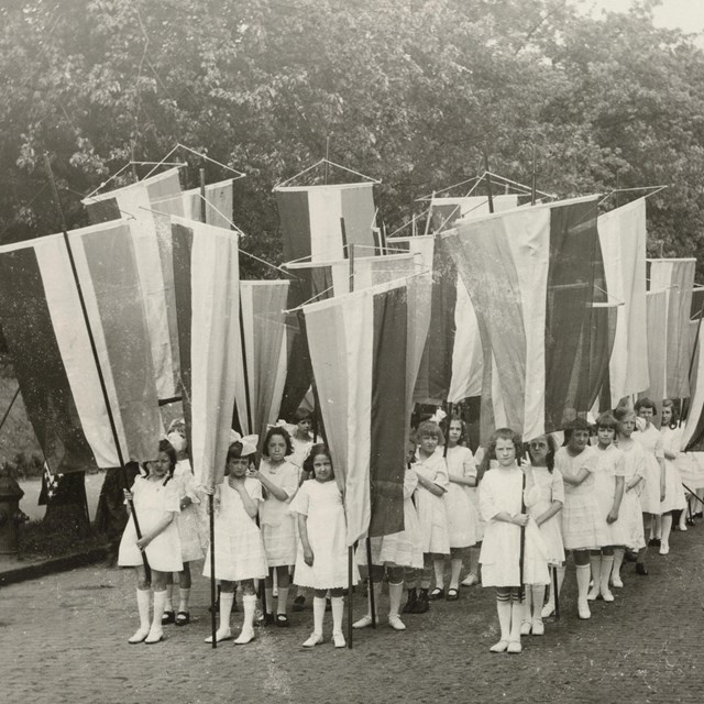 A group of girls wearing white dresses holding suffrage banners