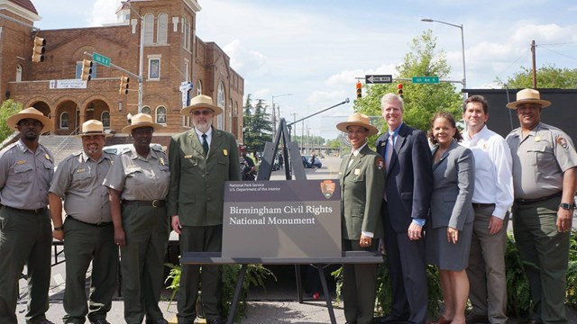 A line of people stand on both sides of a sign that reads Birmingham Civil Rights National Monument.