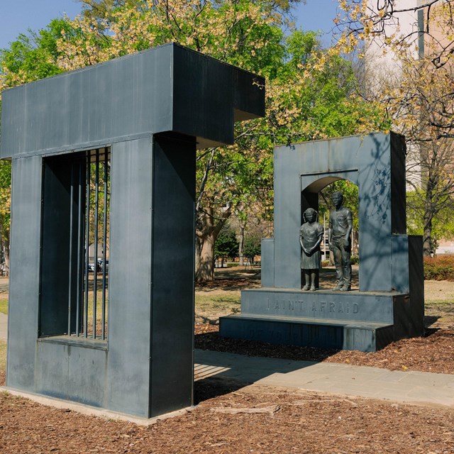 A metal statue of a girl (left) and boy (right) stand above the words 