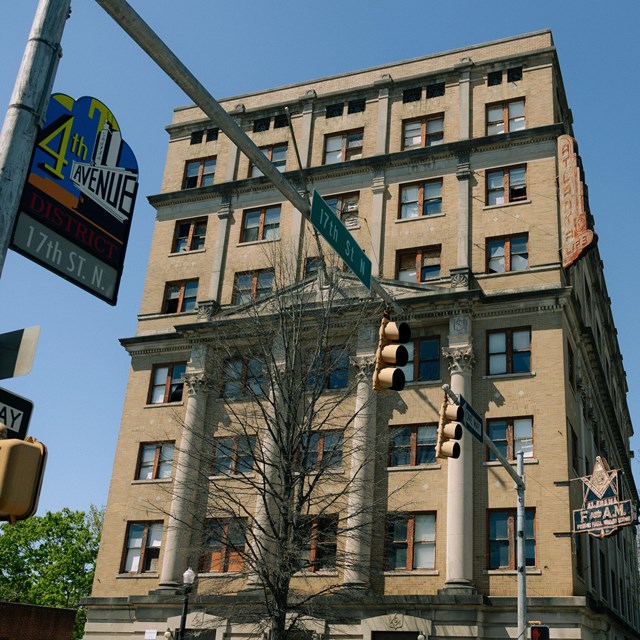 A sign reading 4th Avenue sign hangs in front of a decorative stone building with a masonic symbol.