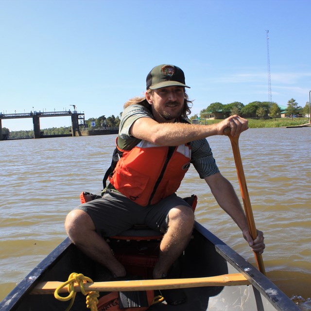 park ranger wearing an orange life jacket paddling a canoe on a river