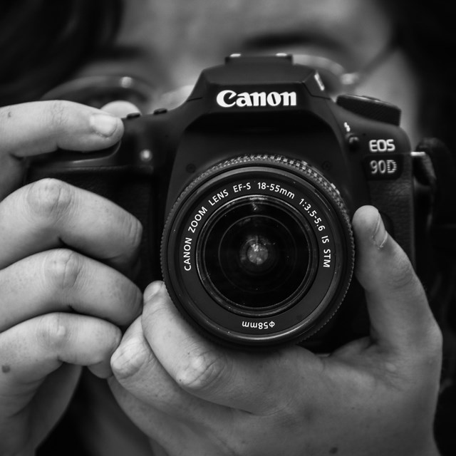 black and white photo of a person pointing their camera at the viewer.