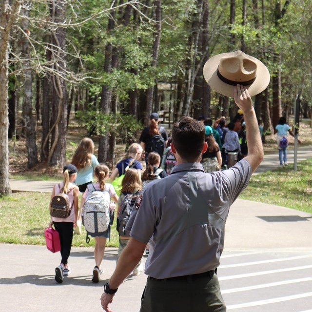 A Park Ranger waves his hat goodbye to students as they walk away from the visitor center