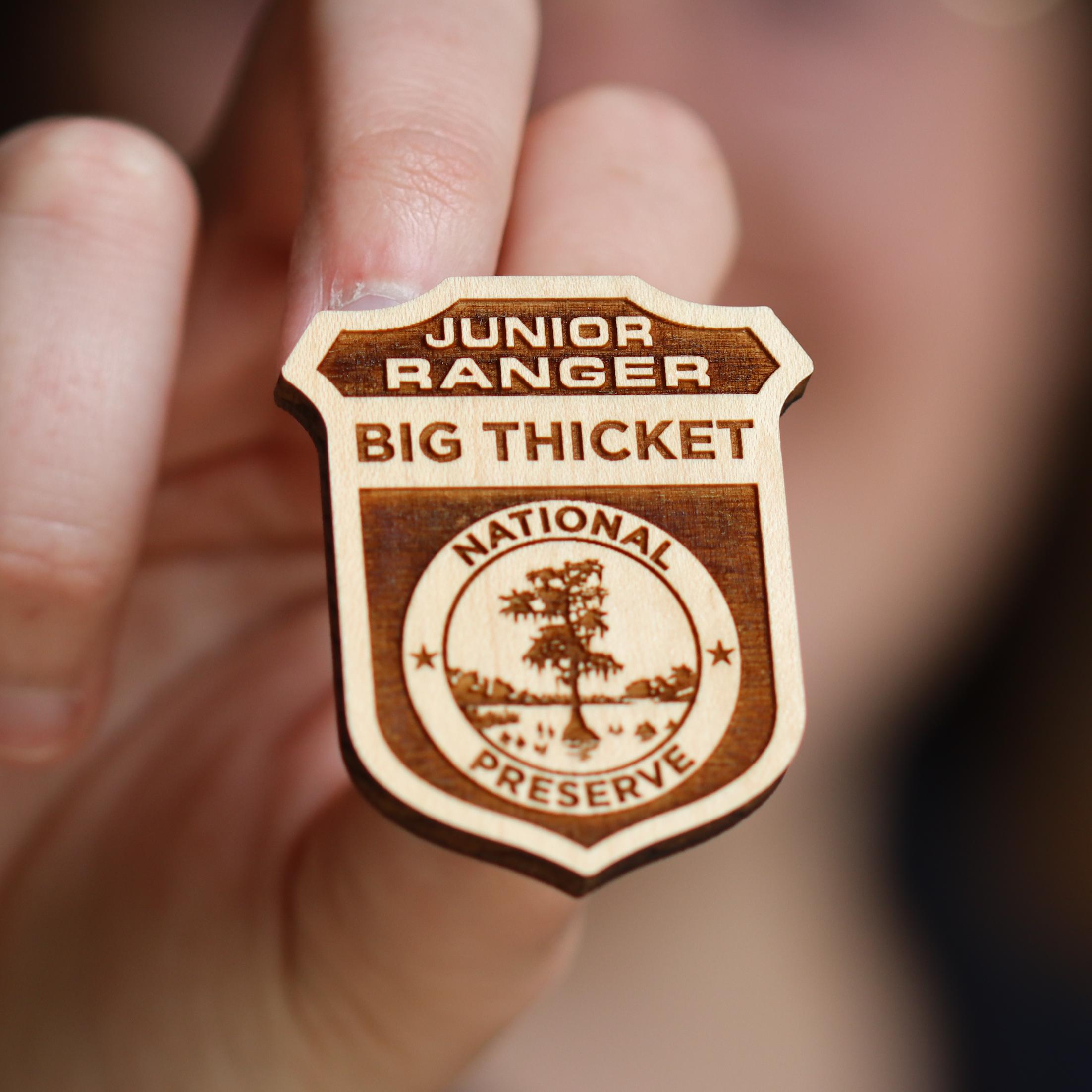 A close-up of a hand holding a wooden Big Thicket Junior Ranger Badge.