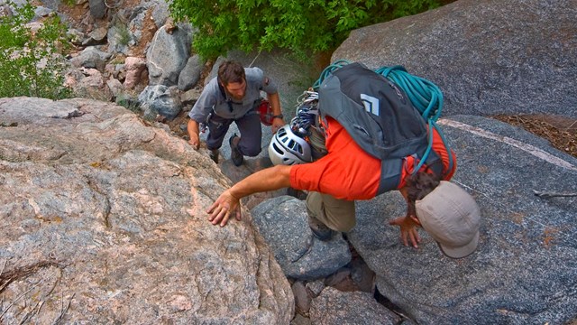 three hikers scrambling up steep rock ledges, viewed from above