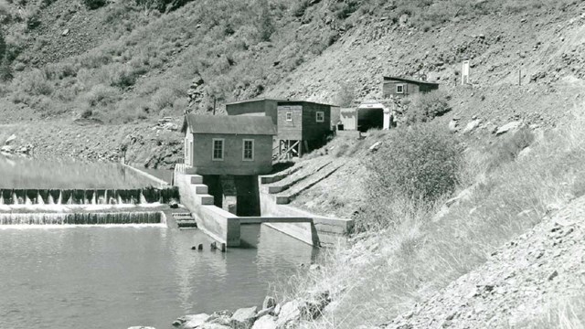 A historic black and white image of a diversion dam and associated buildings in a canyon