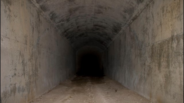 Concrete lined tunnel entrance with a dark center. No light shines through to the other side.