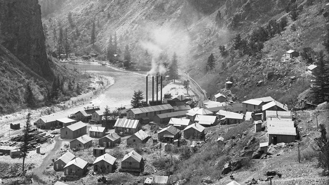 Historic black and white image of a town set on a canyon slope next to a river.