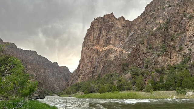 View of a river running through a steep canyon. Vegetation lines the riverbank.