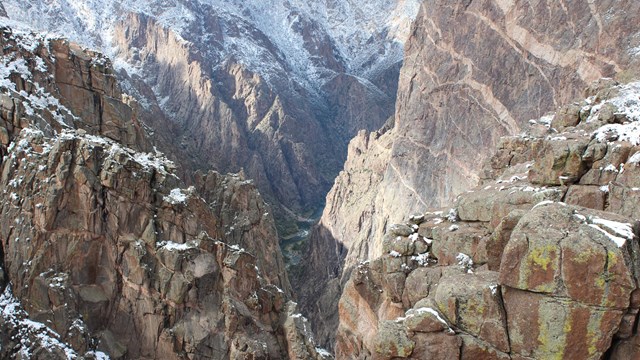 Steep crags dip toward the river, light colored rocks streak the darker canyon wall, snow behind