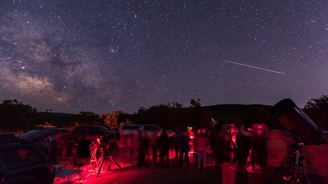 people around telescopes under a starry night sky