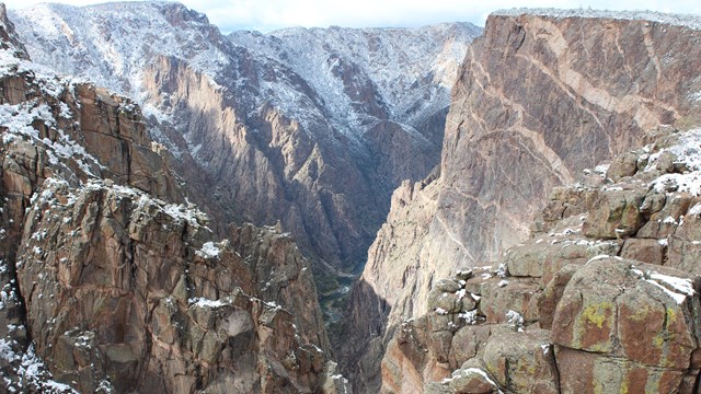 Steep, deep canyon walls with snow on the rim and shaded slopes. Pegmatite ntrusions are visible.