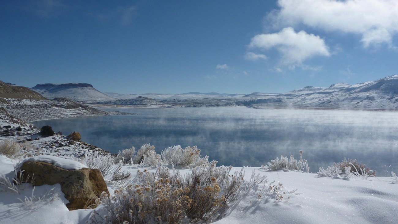 Winter scene with snow covering sagebrush and mesas. A large reservoir is in between.