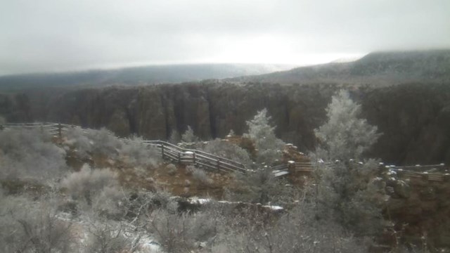 Screenshot image of a canyon and fence-lined trail with patches of snow