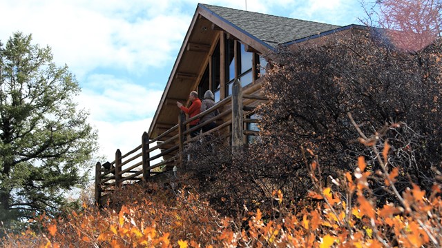 A wooden cabin style visitor center with people walking towards it and a flag flying above