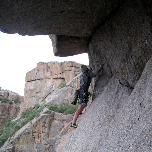 a rock climber clinging to a gray rock wall under a large overhang