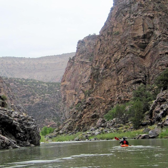 a kayaker on calm river water with dark canyon walls on either side