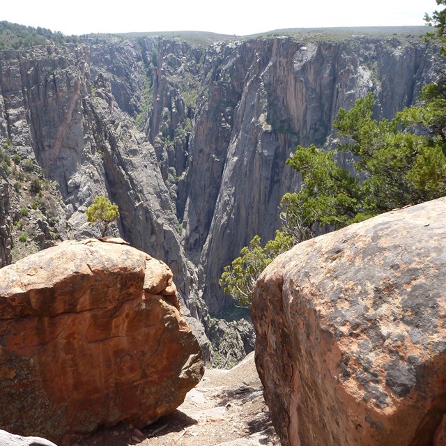 Reddish brown boulders on a canyon wall cliff. Steep, darker canyon walls are in the background.