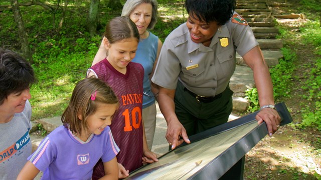 A ranger pointing out some information to four visitors on an outdoor exhibit panel