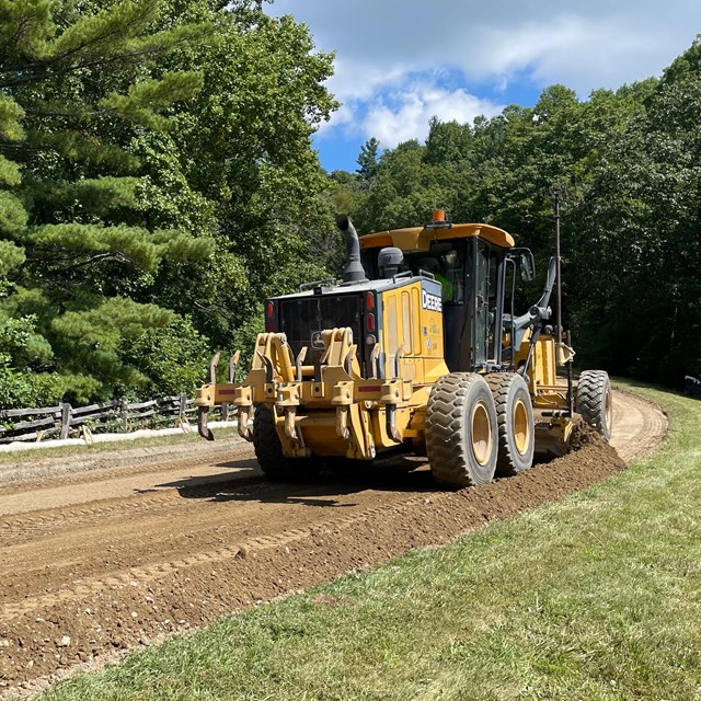 A yellow construction vehicle sits on an unpaved section of the Blue Ridge Parkway.