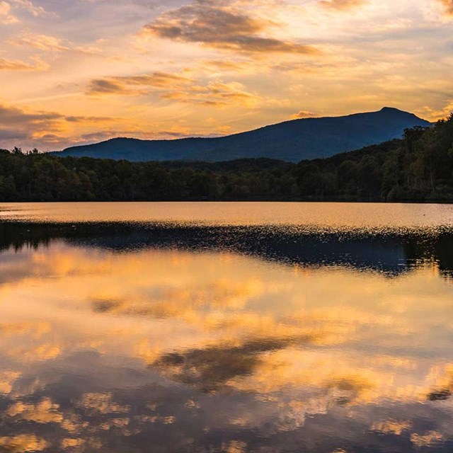 A pink and indigo sunset is reflected in Price Lake with mountains in the background.